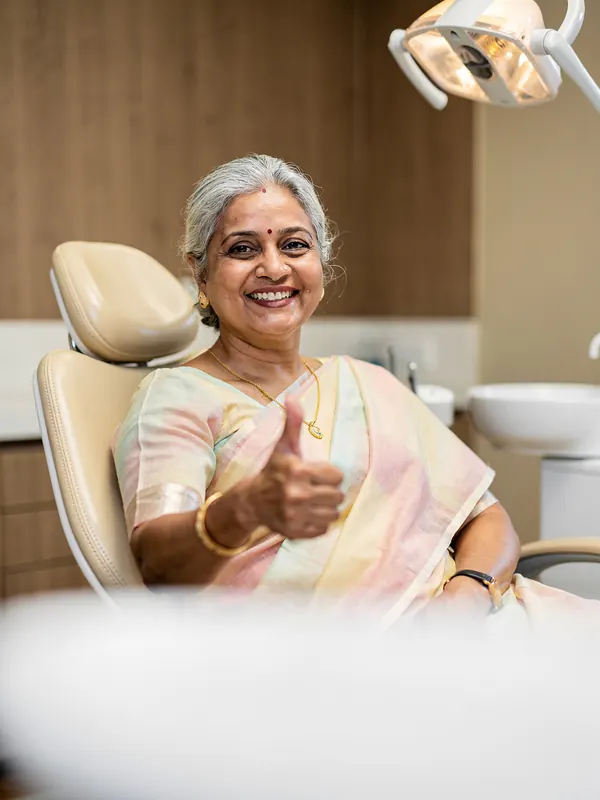 Illustrative picture: a smiling woman in her sixties giving a thumbs up in a dental chair