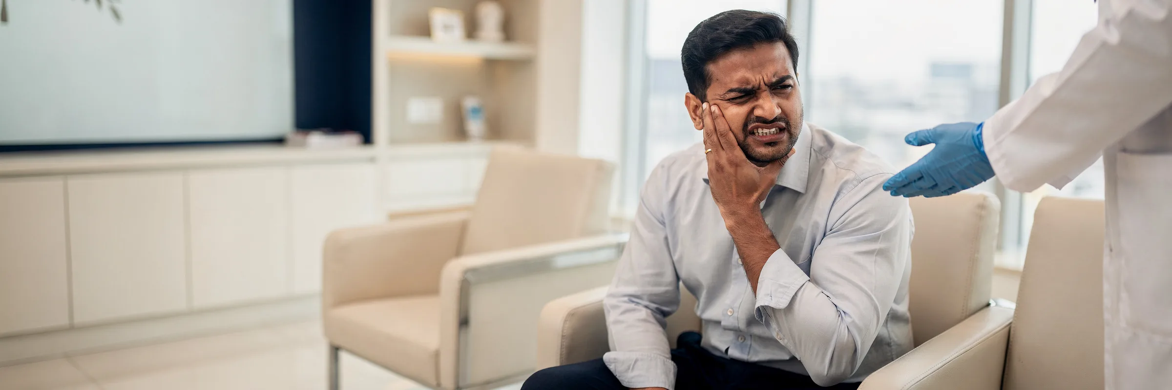 Illustrative picture: a man pressing his jaw in sudden tooth pain as a dentist reaches out to help