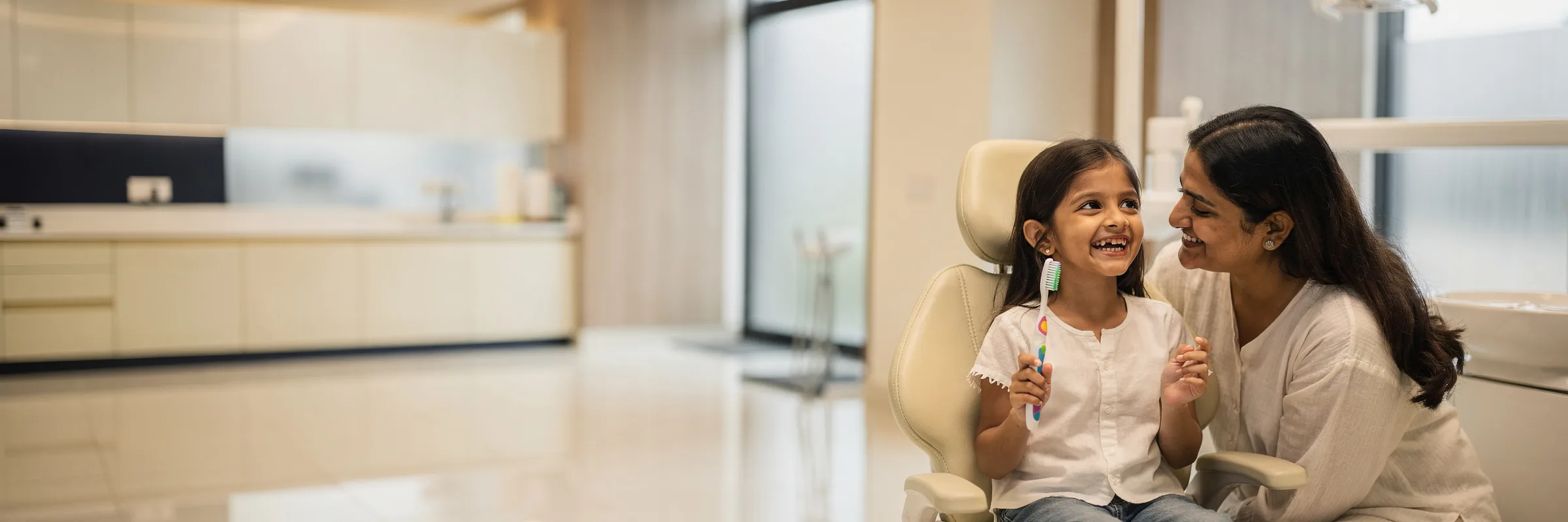 Illustrative picture: a girl laughing in a dental chair with her mother beside her
