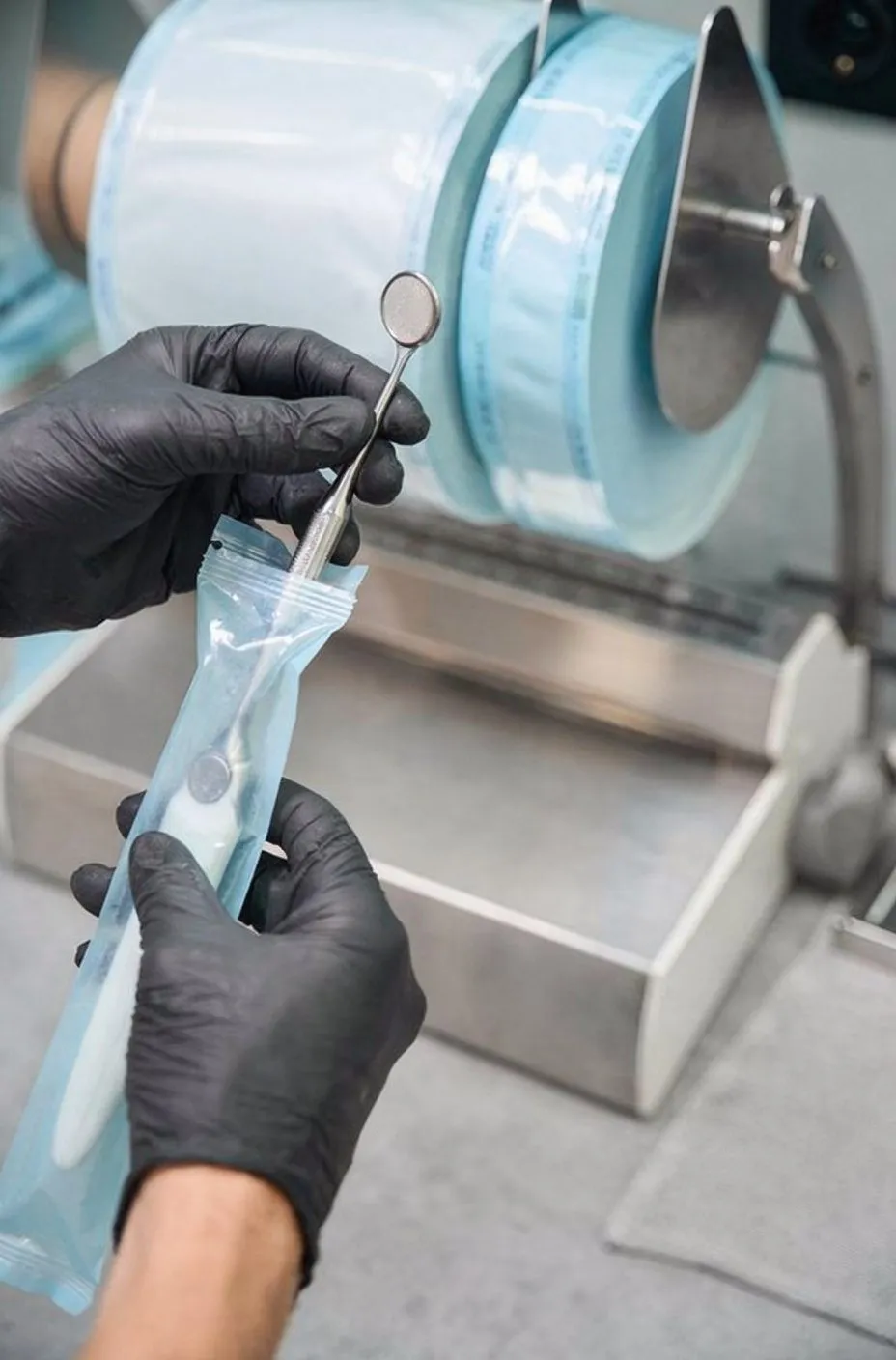 Gloved hands removing dental mirror from sterile autoclave pouch; clinical, hygienic mood
